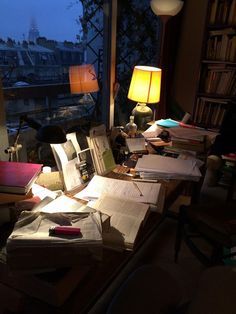 a cluttered desk with books and papers on it in front of a large window