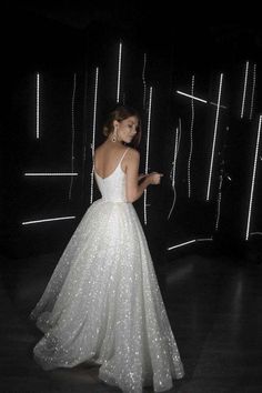 a woman wearing a white dress standing in front of a black wall with lights on it