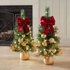 two small christmas trees with red bows and gold ornaments are sitting on a wooden floor