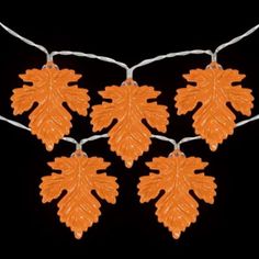 four orange leaves are hanging from a string on a black background and there is no image to describe