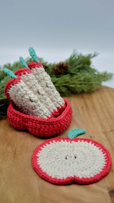 two crocheted apples sitting on top of a wooden table next to pine needles