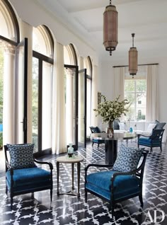 a living room filled with blue chairs and tables next to large window covered in curtains