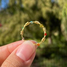 a person is holding a small beaded ring in their left hand, with trees in the background