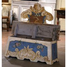 an old wooden bench with blue and gold paint on it's sides in front of a fireplace