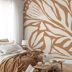 a bed sitting under a window next to a wall covered in brown and white leaves