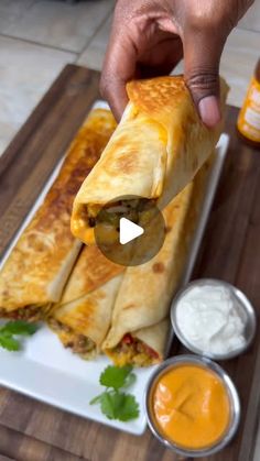 a person is holding up a burrito on a white plate with sauces and condiments