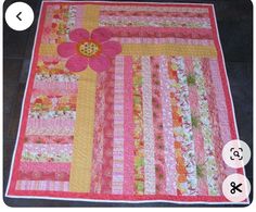 a pink and yellow quilt with flowers on the front, sitting on a black floor