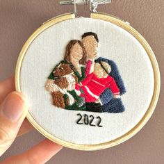 a hand holding a small embroidery hoop with two people and a dog