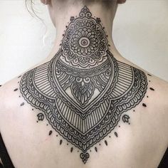 a woman's back neck with an intricate tattoo design on the upper part of her body