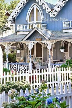 a blue house with white picket fence and flowers in the foreground, on a sunny day