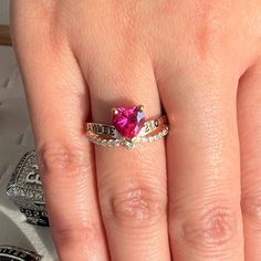 a woman's hand with a pink heart shaped diamond ring on it and the word love is written in cursive writing