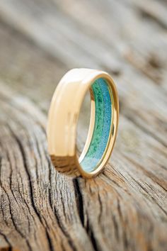 a gold ring with blue and green enamel inlays sits on a piece of wood