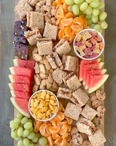 a wooden platter filled with fruit and crackers next to watermelon slices