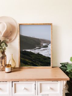 a white dresser topped with a framed photograph next to a vase filled with flowers and a hat