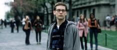 a man with glasses is standing in front of a group of people on the sidewalk