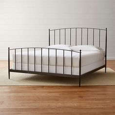 an iron bed frame with white sheets and pillows on top of the bed in a room