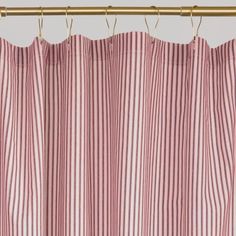 a pink and white striped curtain hanging from a metal rod with two gold hooks on it