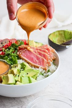 someone pouring dressing on a salad with avocado, tomatoes and other foods in bowls