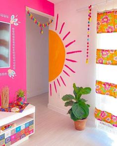 a living room with pink walls and colorful decorations on the wall, potted plant in front of window