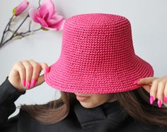 a woman wearing a pink crochet hat with her hands on her head and one hand holding the top of her hair