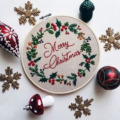 a cross stitch christmas ornament surrounded by other holiday ornaments and baubles