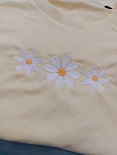 an embroidered t - shirt with three daisies on it