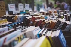 rows of books are lined up on the table in front of people at an outdoor book sale