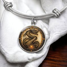 "Year of The Dragon Bracelet, a standout piece in Chinese Zodiac Animal Jewelry, serves as a symbolic Gift and Spirit Companion, featuring an Engraved Charm Pendant to celebrate the Lunar New Year 2024, embodying the strength and wisdom of the dragon. ➜ Our Dragon Jewelry is Not 3D, it's made of high quality surgical steel with a graphic image that's printed directly onto the steel surface with a shatterproof liquid glass coating and includes an 18k gold finish option. ➜ Our Engraved Dragon Pend Symbolic Metal Bracelets, Symbolic Round Metal Bracelet, Symbolic Zodiac Sign Collectible Jewelry, Zodiac Sign Bracelet Jewelry Gift, Symbolic Zodiac Sign Jewelry, Collectible Round Zodiac Sign Jewelry, Round Zodiac Sign Jewelry Collectible, Round Spiritual Collectible Bracelets, Symbolic Zodiac Sign Bracelet Jewelry