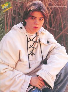 a young man sitting on the ground wearing a white jacket