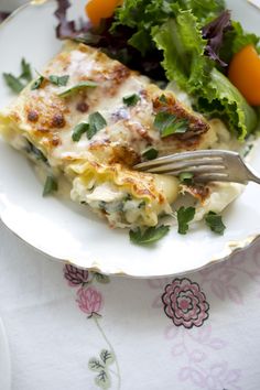 a white plate topped with lasagna covered in cheese and veggies next to a salad