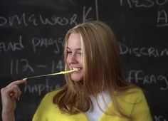 a woman holding a pencil in front of a blackboard