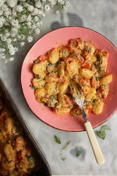 a pink plate topped with pasta next to a casserole dish