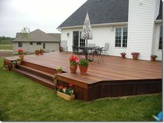 a wooden deck with potted plants on it in front of a white house and lawn