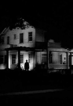 a person standing in front of a house at night with the light on and behind him