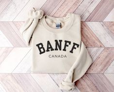 Explore winter warmth with our stylish Banff sweatshirt--a fusion of minimalistic chic and cozy fleece lining. Embrace the bold varsity font, available in either black or white to complement your chosen top color. This aesthetically pleasing and adorable crew neck sweater makes an ideal gift for snowboarders, skiing enthusiasts, and lovers of winter sports. It's also the perfect companion for those planning a trip to Canada, particularly the picturesque town of Banff. Indulge in both fashion and Banff Sweatshirt, Banff Vacation, Apres Ski Bachelorette, Aesthetic Canada, Ski Bachelorette, Minimalistic Chic, Trip To Canada, Varsity Font, National Park Shirt