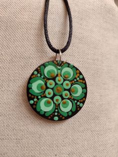 a green and brown circular pendant on a black leather cord with an oval design in the center