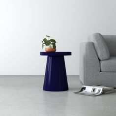 a blue table with a plant on it next to a gray couch and white wall