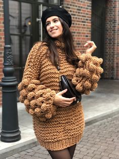 a woman is walking down the street with her hand in her pocket and wearing a knitted sweater