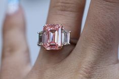 a close up of a person's hand with a pink diamond ring on it