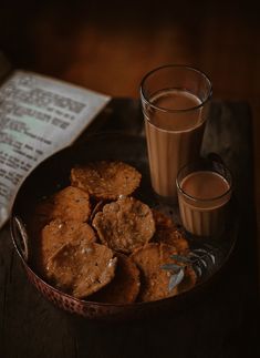 two glasses of milk and some cookies on a plate with newspaper next to it,