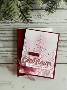 a christmas card with red ribbon on it and pine tree branches in the back ground