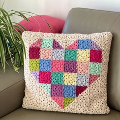 a crocheted heart pillow sitting on a couch next to a potted plant