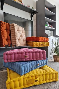 three different colors of pillows stacked on top of each other in front of a television