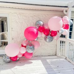 pink and silver balloons are hanging from the side of a house