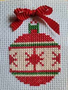 a cross stitch christmas ornament hanging on a white piece of cloth with red ribbon