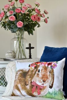 a pillow with a bunny on it sitting next to a vase filled with pink roses