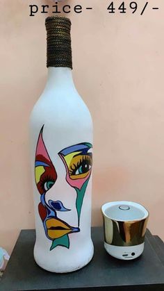 a white bottle with a face painted on it next to a cup and saucer