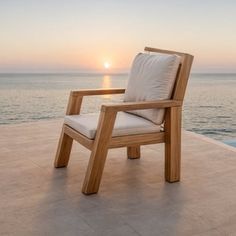 a wooden chair sitting on top of a stone floor next to the ocean at sunset