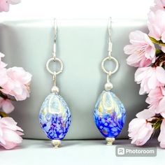 a pair of blue and white glass beaded earrings with silver hooks on them next to pink flowers