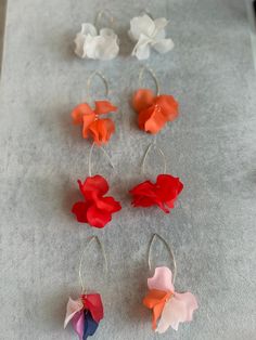 four different colored flowers are hanging from silver hoop earrings on a gray surface with white and red petals